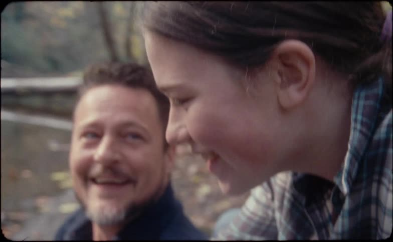 A man a woman and a girl by a pond talking and laughing