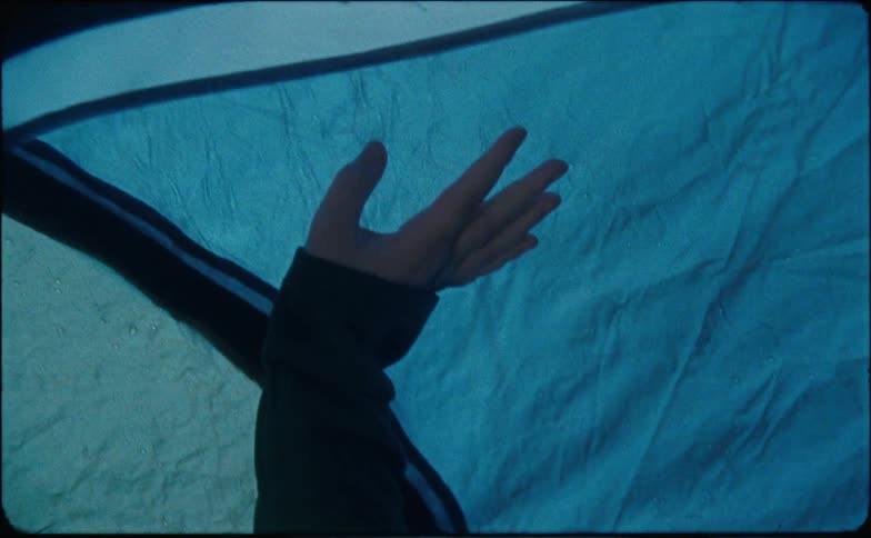 A camper reaches up to touch the inside of a tent while rain water pours down