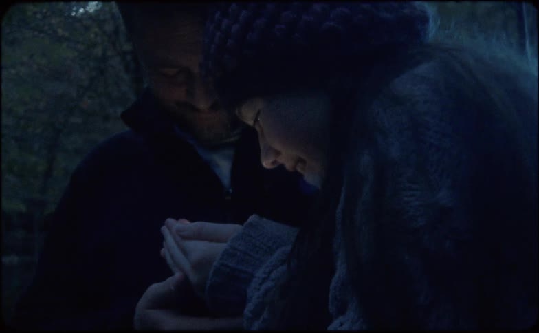 A young girl smiles at her father as she holds a glowing firefly in her hands