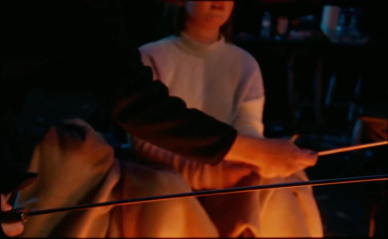 A father shows his son how to hold a skewer over a campfire