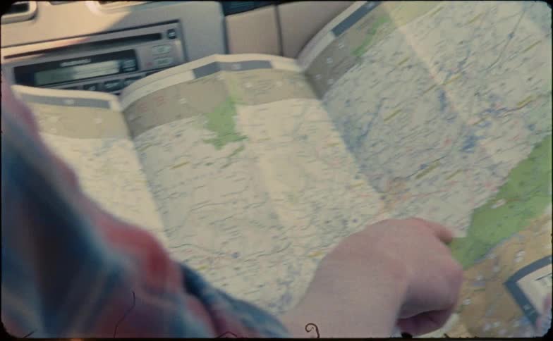Two people hold a large road map and point and discuss routes