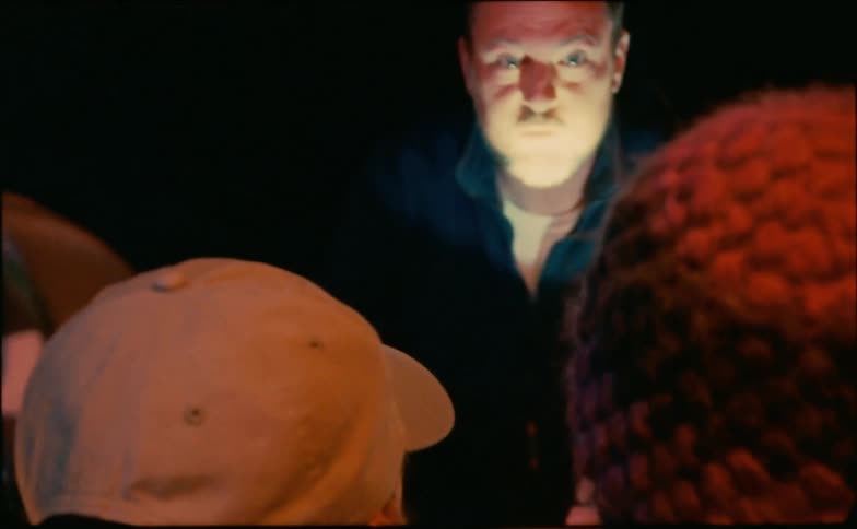 A man tells a scary story to a group of children by the light of a flashlight