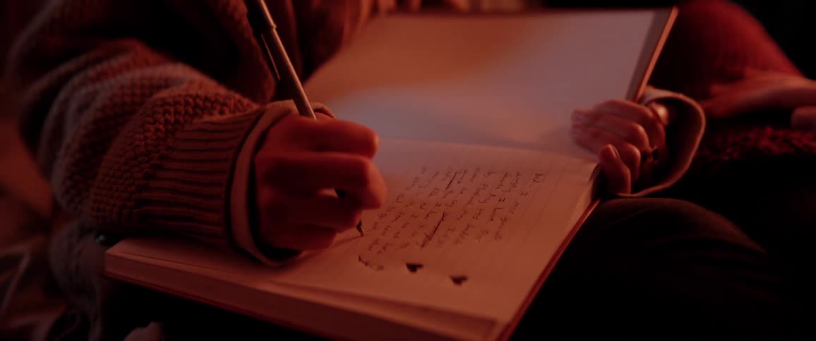 White woman writing on her notebook close to a fire place