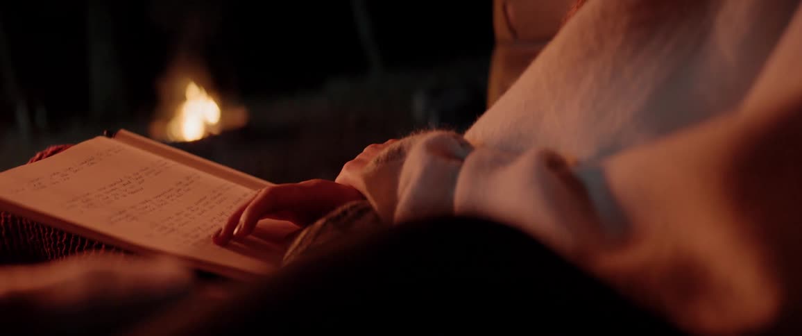 White woman reading a book while sitting inside a car close to a camp fire