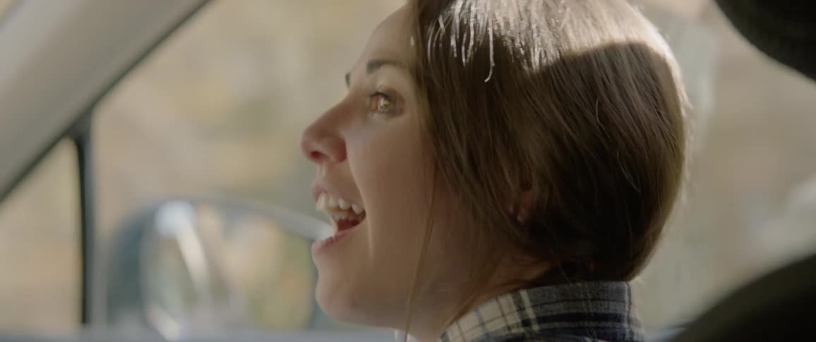 Female in the passenger seat of a moving vehicle is smiling and talking with the driver as they travel down the road