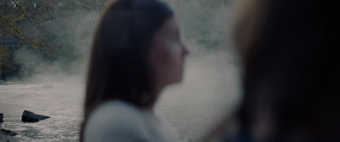 Two women stand next to a river and talk