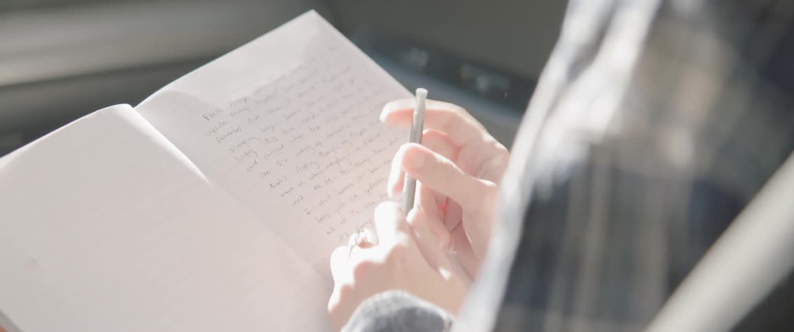 A person sits in the passenger seat of a vehicle with a pen and notebook