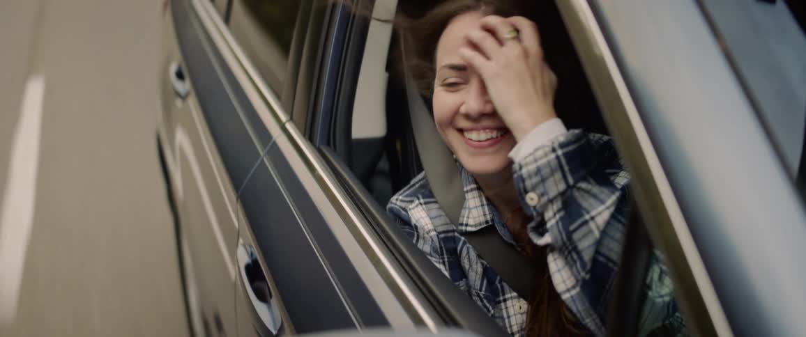 A young woman resting her head on the window sill in the passenger seat of a moving vehicle