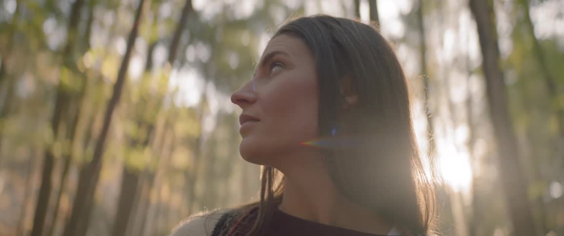 A woman gazing around herself as she stands in a forest