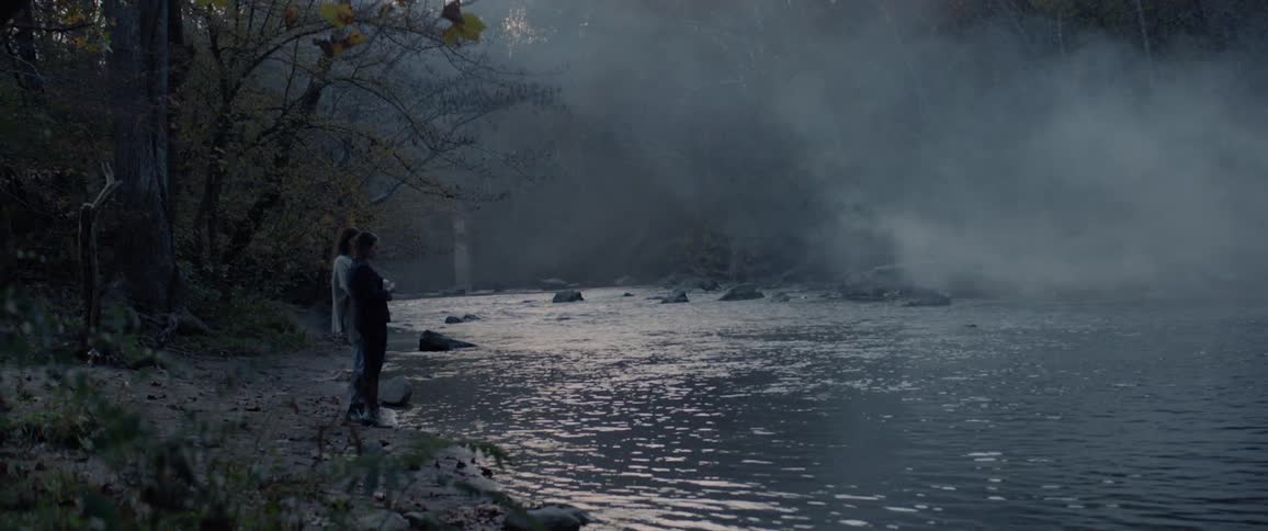 Two women standing near a riverbed in middle of a forest
