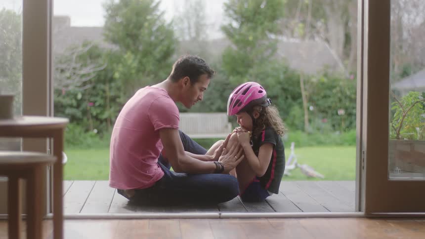 A father kisses his daughters injured knee from bike riding
