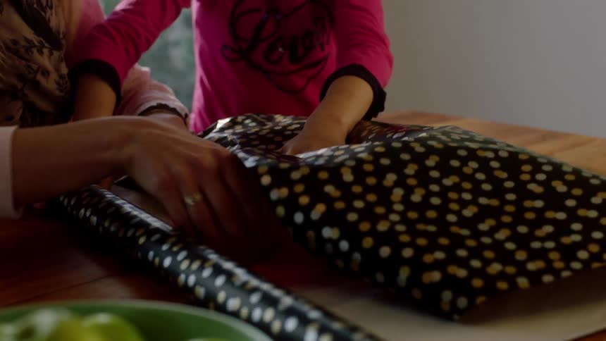 Mom and daughter wrap a present in a room