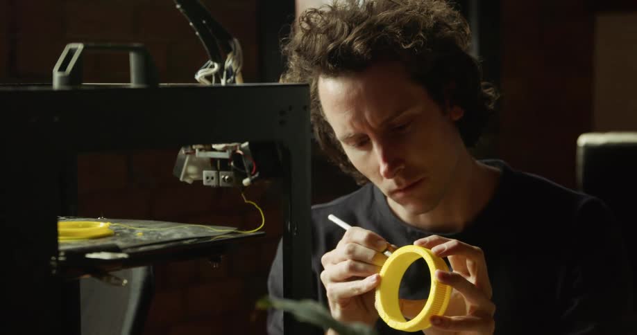 A man in front of a 3d printer writing on a yellow plastic cylinder