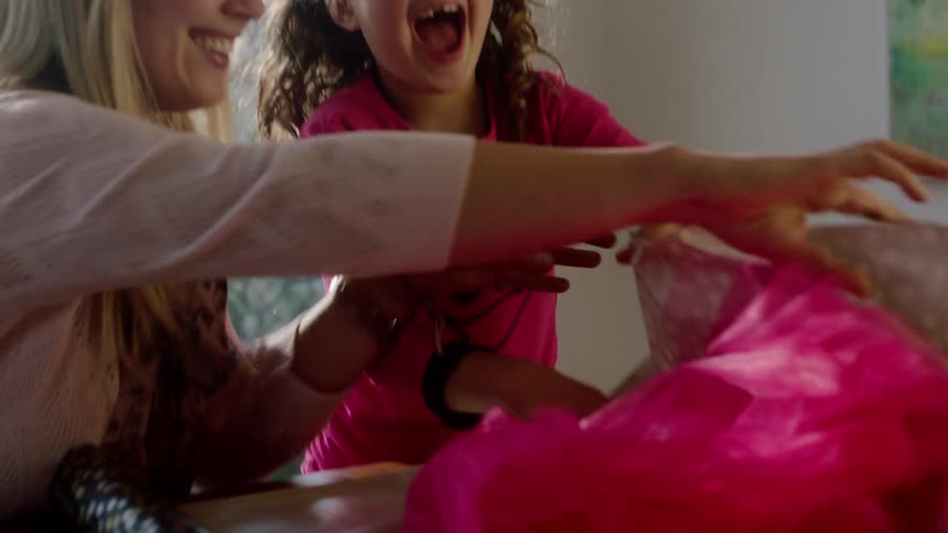 Mother and daughter having fun together while packing a gift at the table
