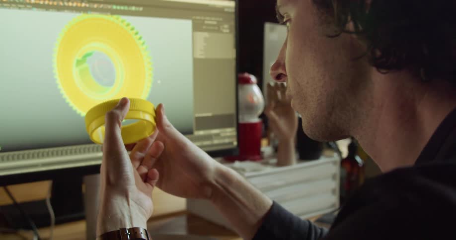A man sitting at a computer is comparing an object in his hand to a 3d version of the object in cad software