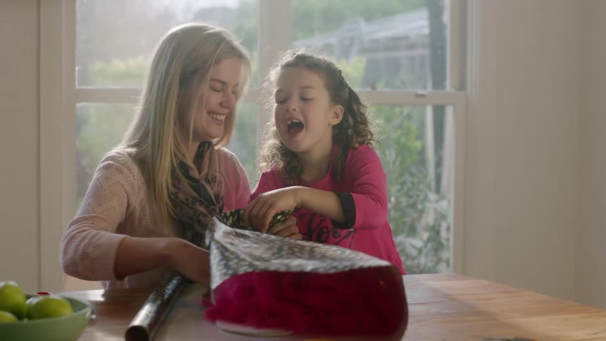 Little girl happily packing a gift with her mother on a table