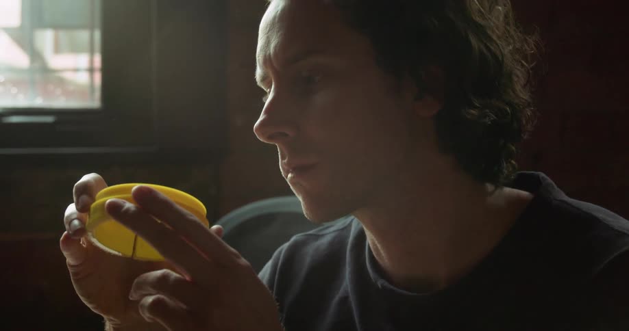 A man sitting on a chair next to a 3d printer looking at a yellow cylinder