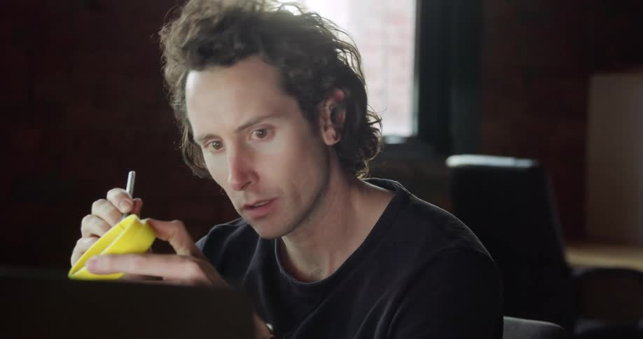 A man looks at his computer while making modifications to a piece of plastic he is holding