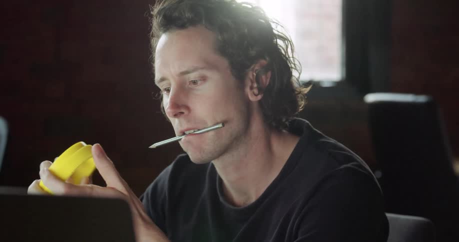 Man looking at instructions on laptop while putting a pen on his mouth and handling a object