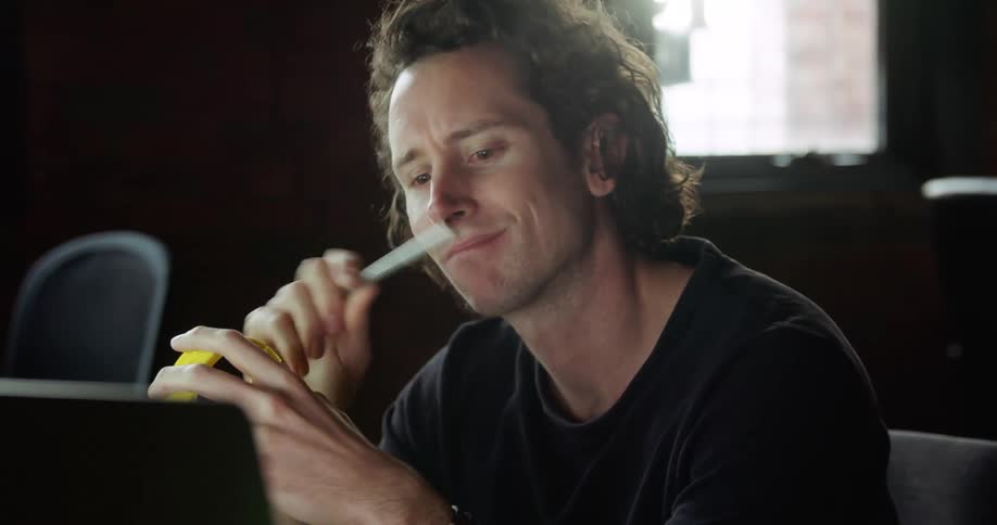 A man sits and thinks at his desk while holding a yellow piece of plastic