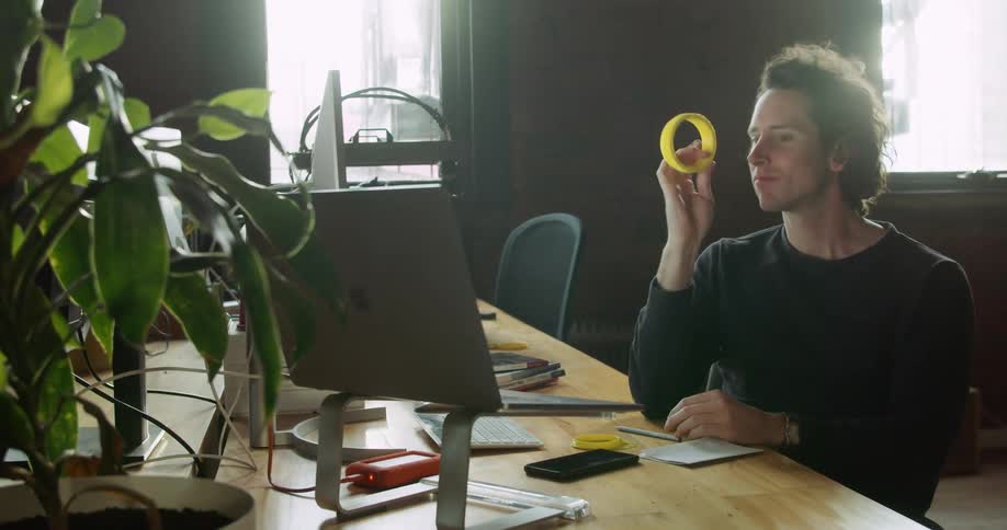 A man at a desk throws up a small yellow object as he thinks hard at his computer desk