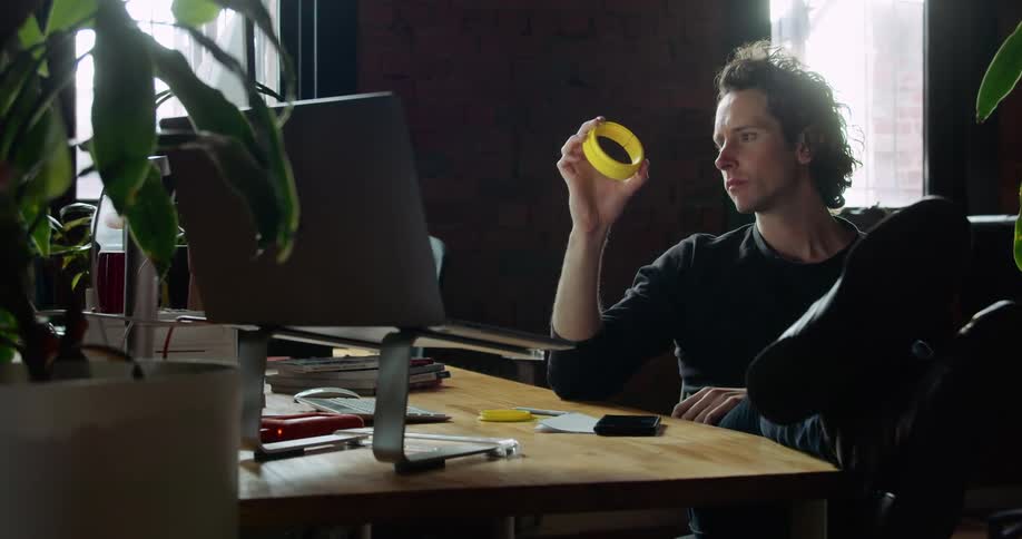A man sitting in a chair at desk examining a plastic yellow object in his hand