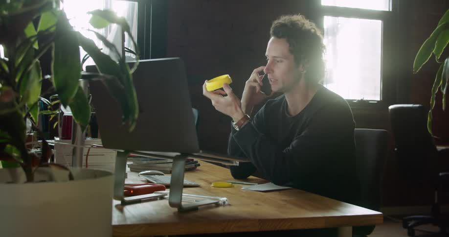 Man sits in office contemplating item and talking on phone
