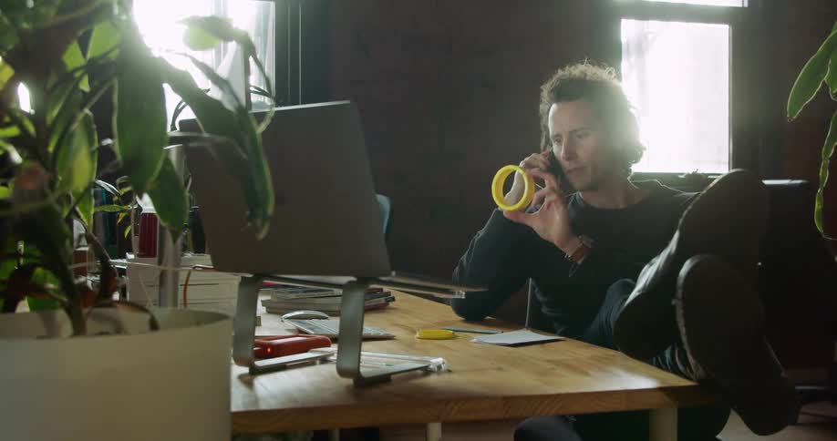 Man leans back in chair in office talking on mobile phone and examining plastic ring