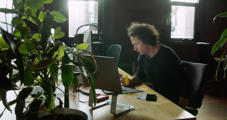A man taking a yellow cylinder from a 3d printer then walking and sitting at a desk