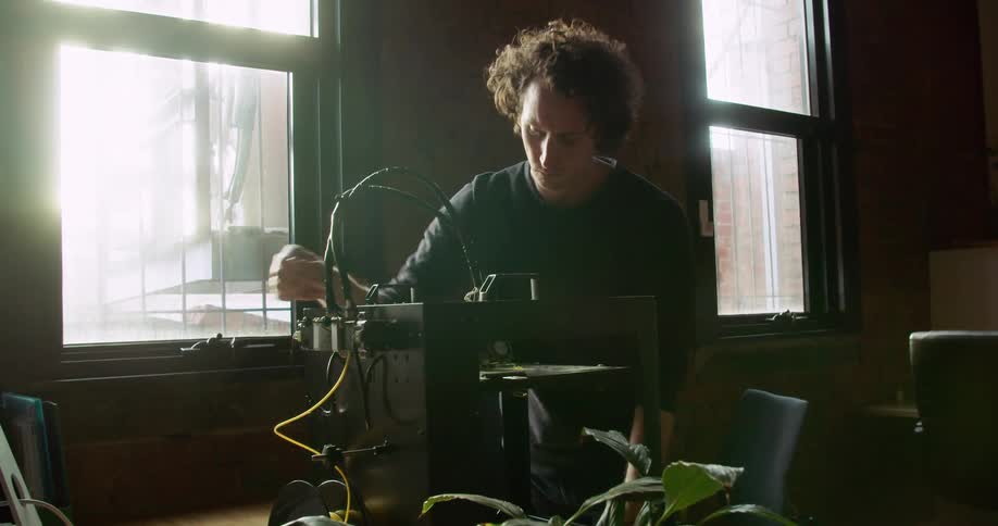 A man standing by a desk adjusting dials on a 3d printer
