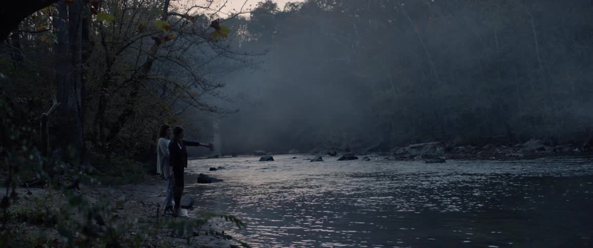 Two women standing at edge of stream pouring ashes out from urn