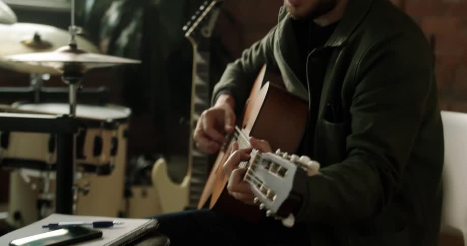 A man turns on his phone and sings while playing the guitar