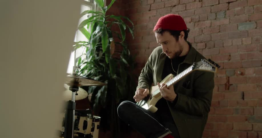 A man sits in a corner and plays an electric guitar
