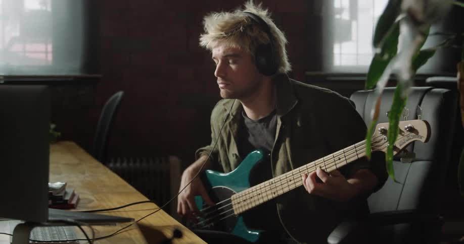 Man sitting at the desk plays and records an bass guitar on a pc computer