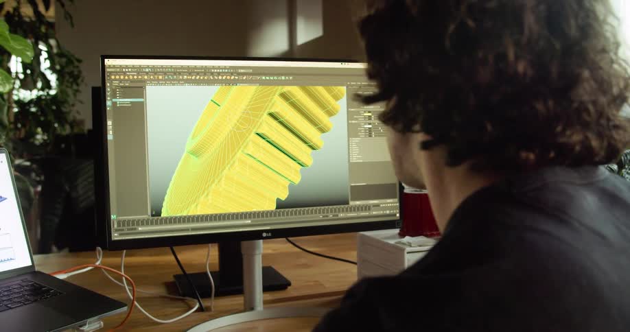 A man sitting at his desk in front of a computer monitor looking at a digital gear