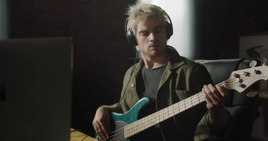 Man sitting at the desk plays and records an electric guitar on a pc computer