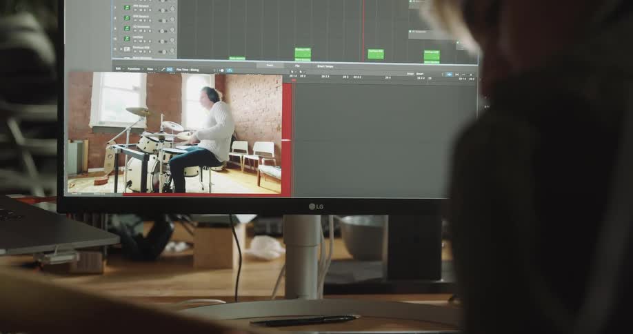 A man sits and faces a computer showing a man playing the drums
