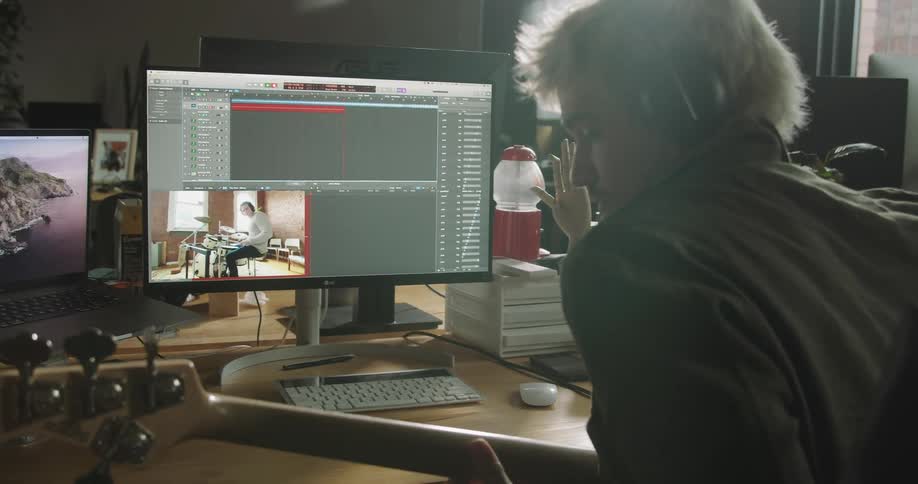 A man plays a guitar sitting at a desk with a computer