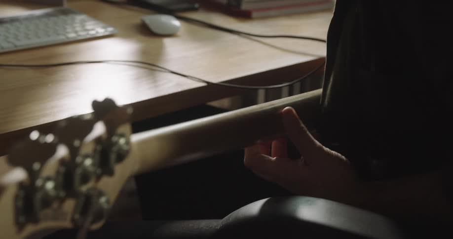 Man sitting at the desk records a bass guitar on a pc computer in the office