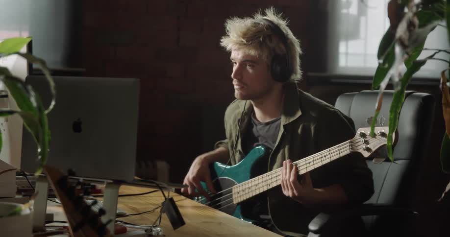 A man sits at a desk with a computer and playing the guitar