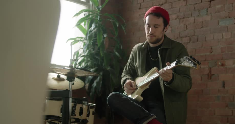 A musician plays the guitar while sitting next to a set of drums