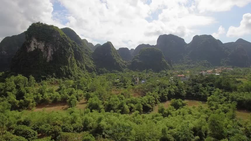 A bus travels on a rural road toward a remote town with rocky formations covered in green