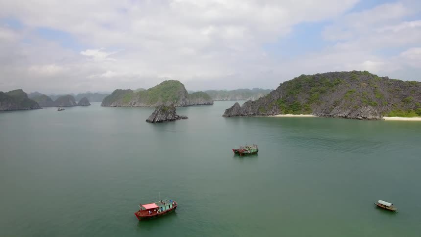Boats float on green tinged ocean among scattered islands