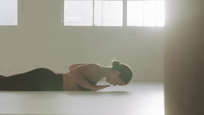 A woman does yoga in an empty room with sun shining through the windows