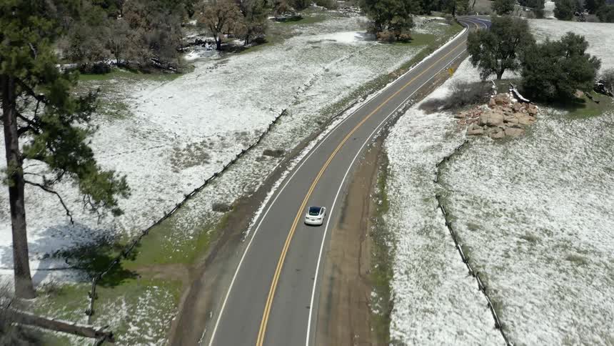 Aerial view of a car driving on the winding road through hills