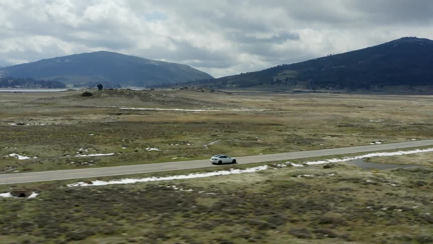 White car driving on an empty road in the middle of a grass field