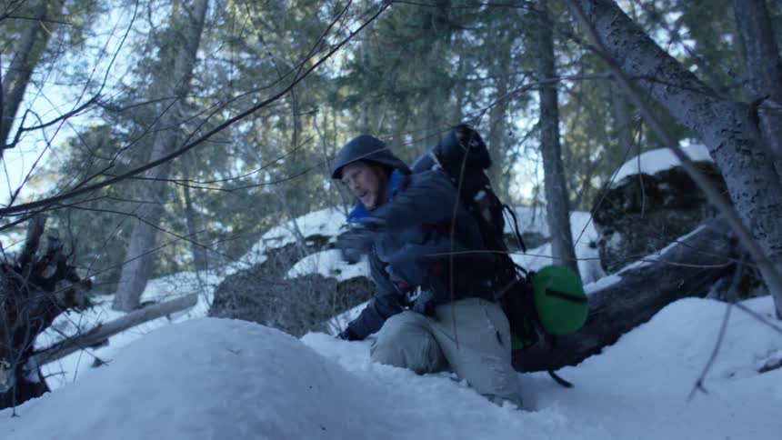 A man struggles to walk through a snow covered woods area