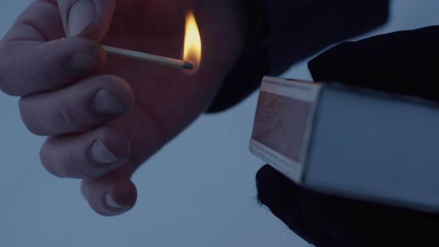 A person striking a match against the side of a matchbox