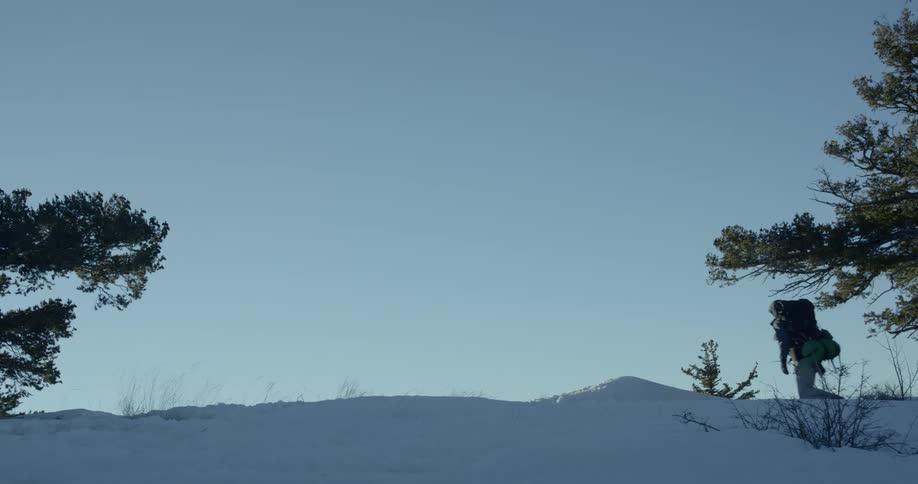Man climbs a snow covered hill on a sunny day