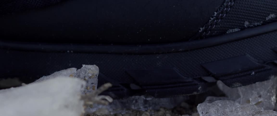 Black shoes sole stepping on ice and breaking it